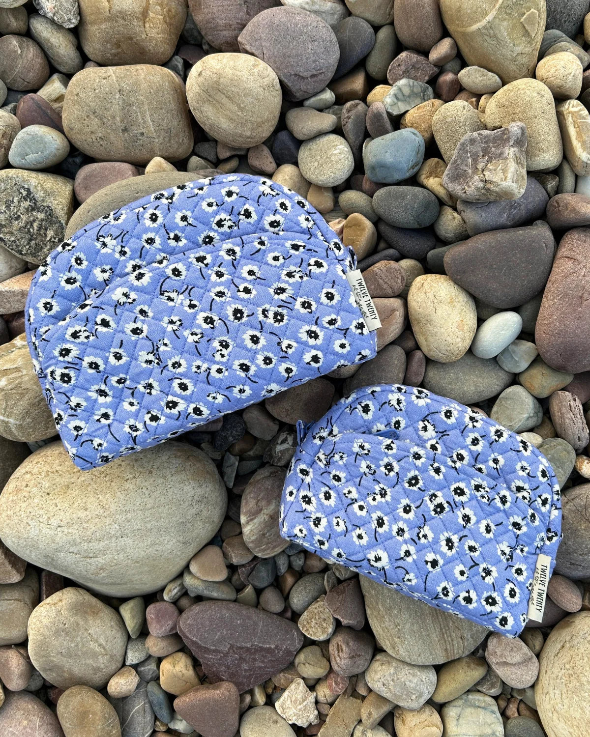 Two blue fabric pouches with white floral patterns on a bed of multicolored stones.