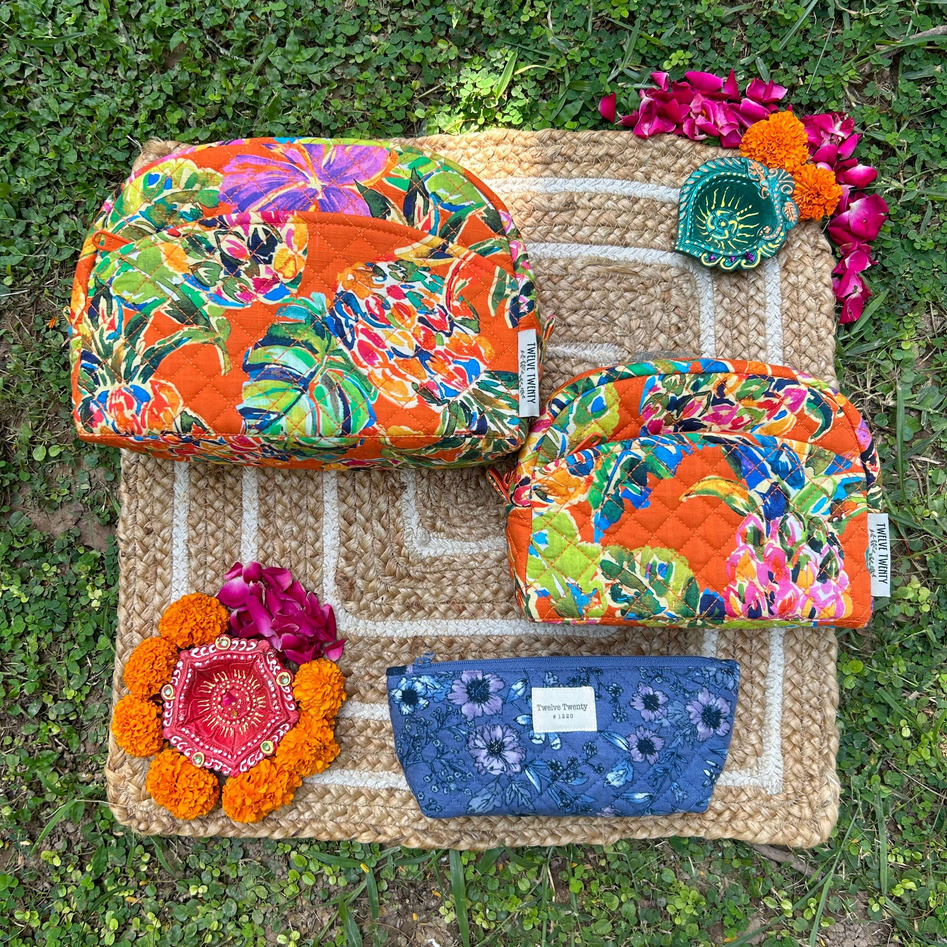 Vibrant Trinity Set of 3 makeup bags and pouches on decorative mat surrounded by flowers, featuring colorful floral designs.