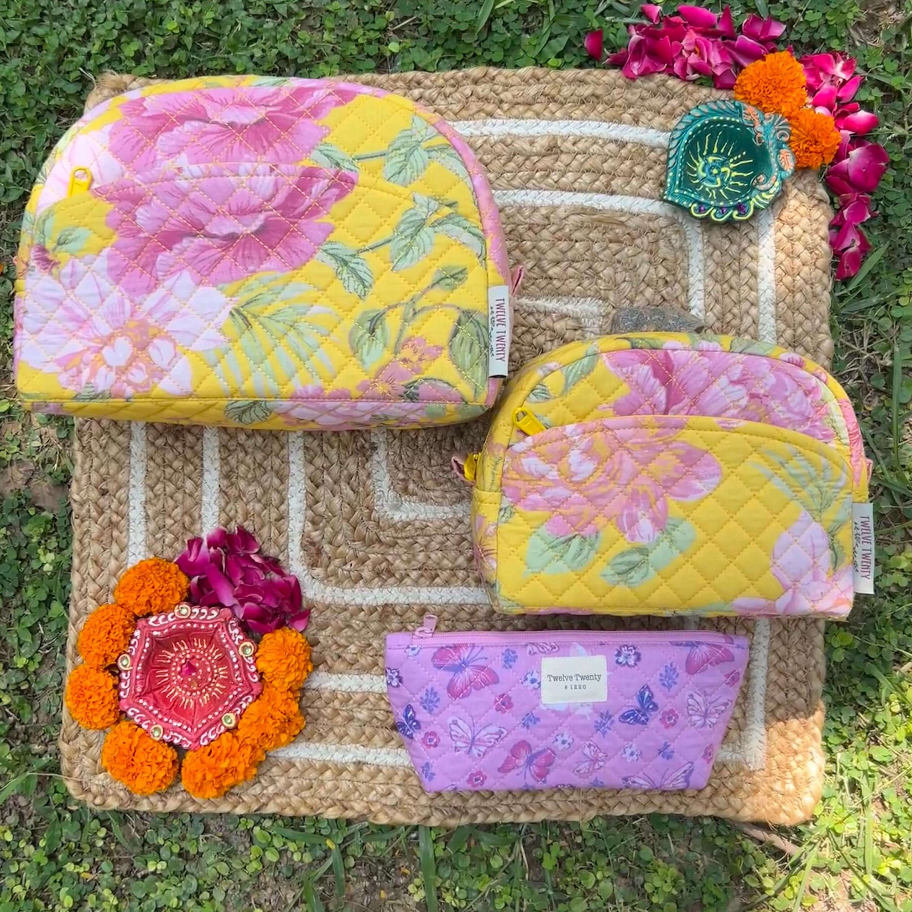 Trinity set of three floral makeup bags and pouches on a woven mat with decorative flowers.