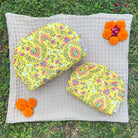 Yellow floral makeup bags set with wipe-clean lining, displayed outdoors with marigold flowers, ideal for travel and everyday use.