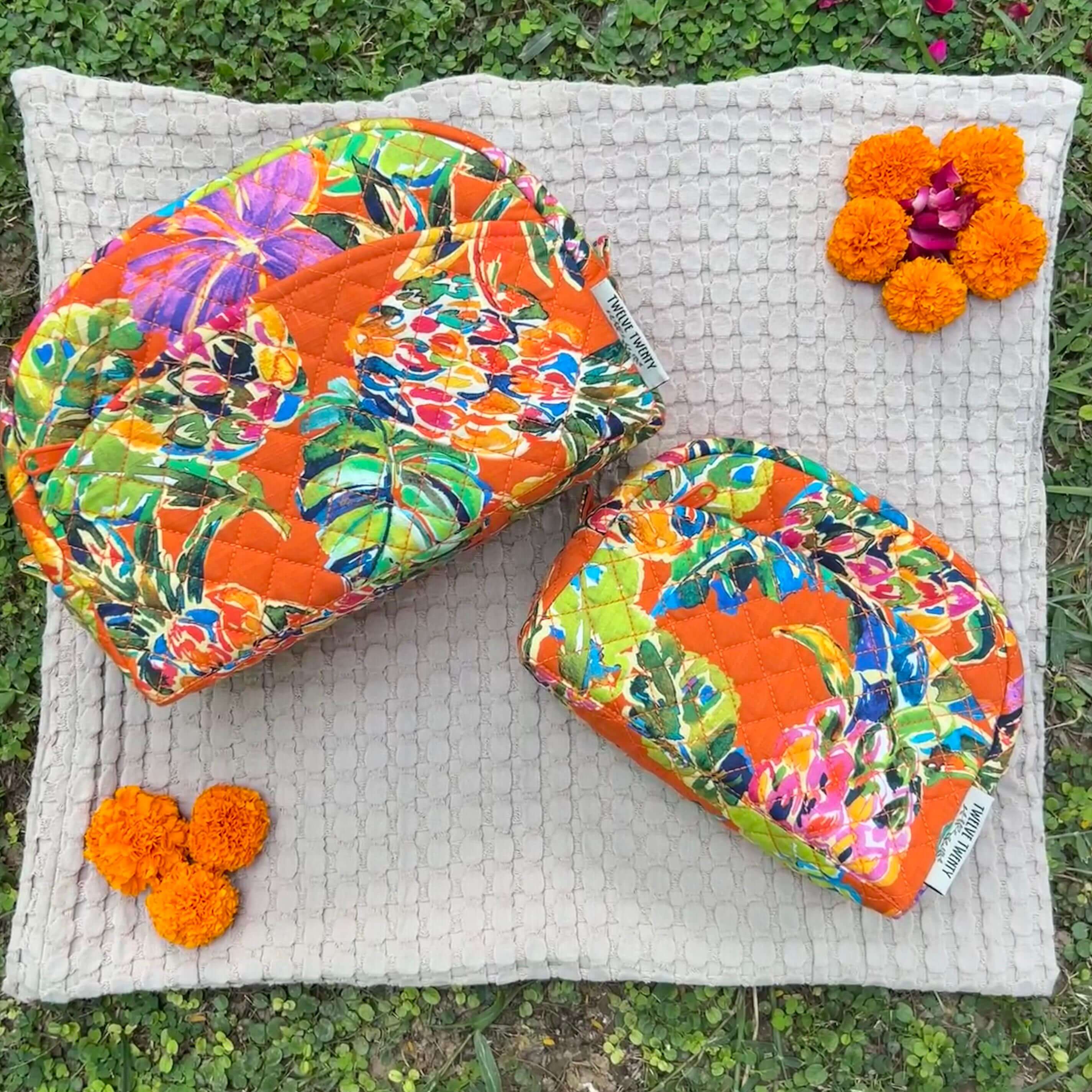 Colorful floral makeup bags set of 2 on a textured mat with marigolds; perfect for travel and everyday cosmetic storage.