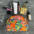 Colorful makeup pouch with various cosmetic products on a dark surface.