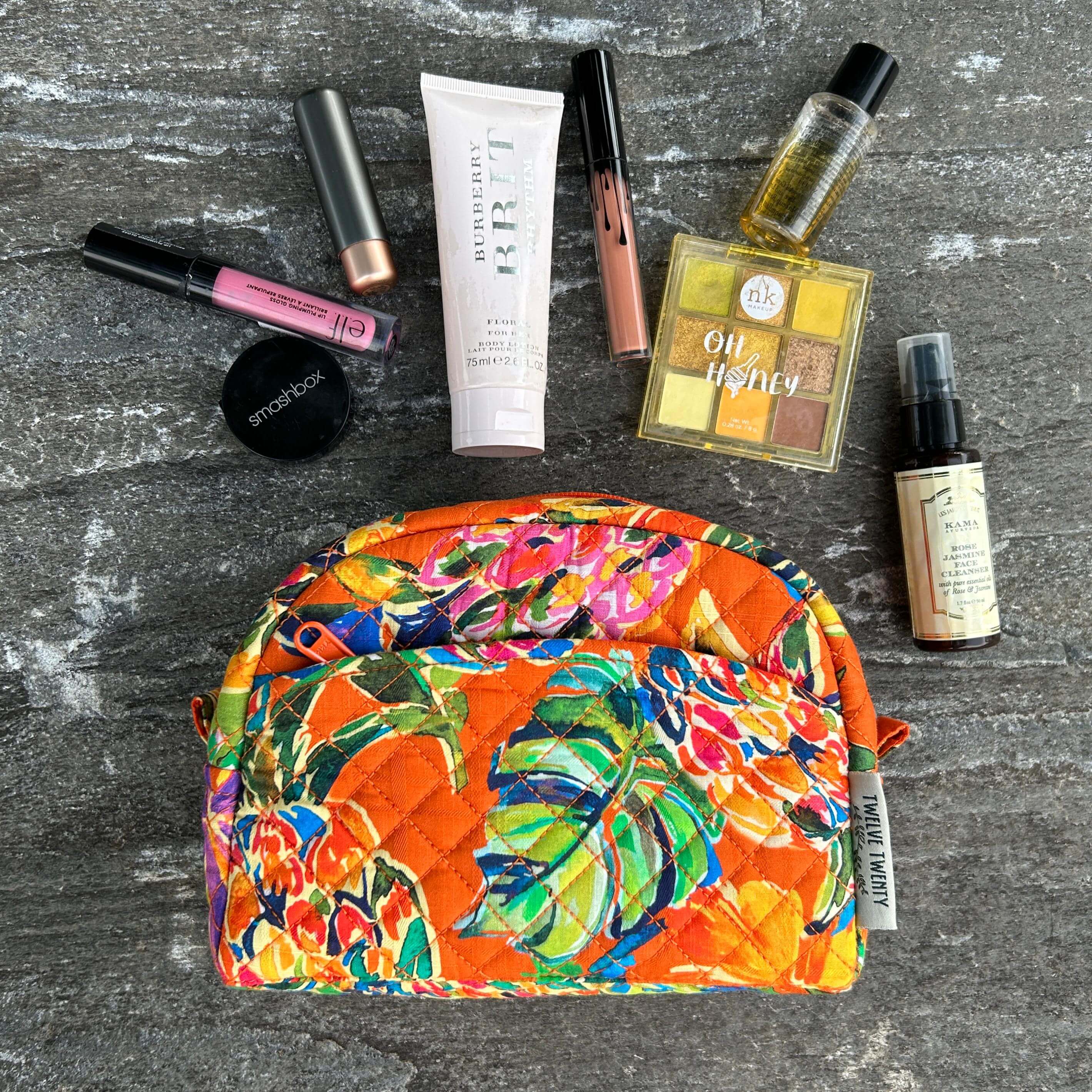 Colorful makeup pouch with various cosmetic products on a dark surface.