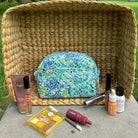 Blue floral makeup pouch with assorted cosmetics displayed on a wicker basket background.