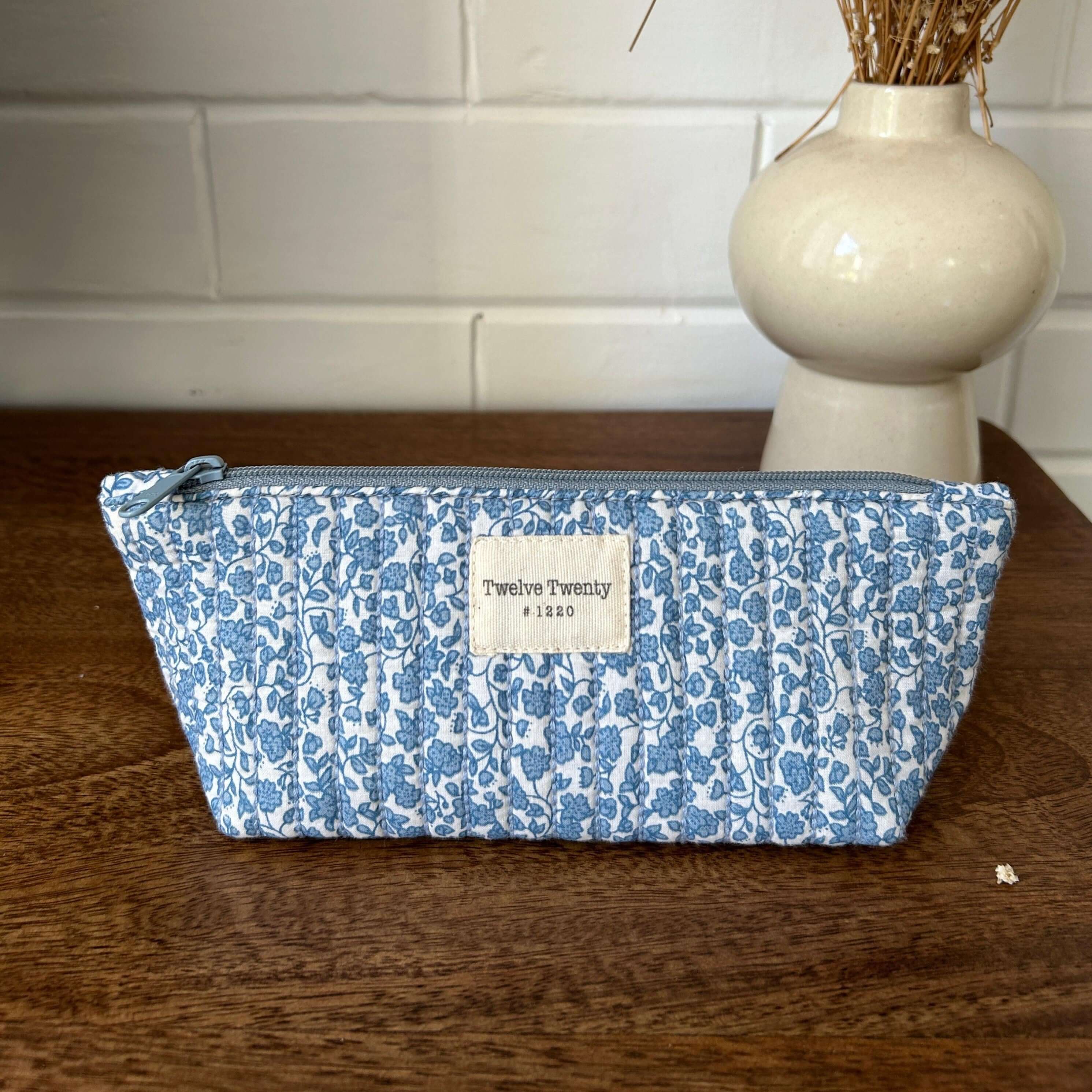 Blue floral cosmetic pouch with zipper on wooden table, ideal for makeup and skincare storage, featuring wipe-easy lining.