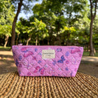 Pink butterfly-patterned makeup pouch on a wicker surface outdoors