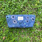 Blue floral makeup pouch with zipper, featuring a quilted design, lying on green grass.