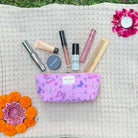 Purple butterfly makeup pouch with cosmetic products on a textured background, surrounded by flowers.