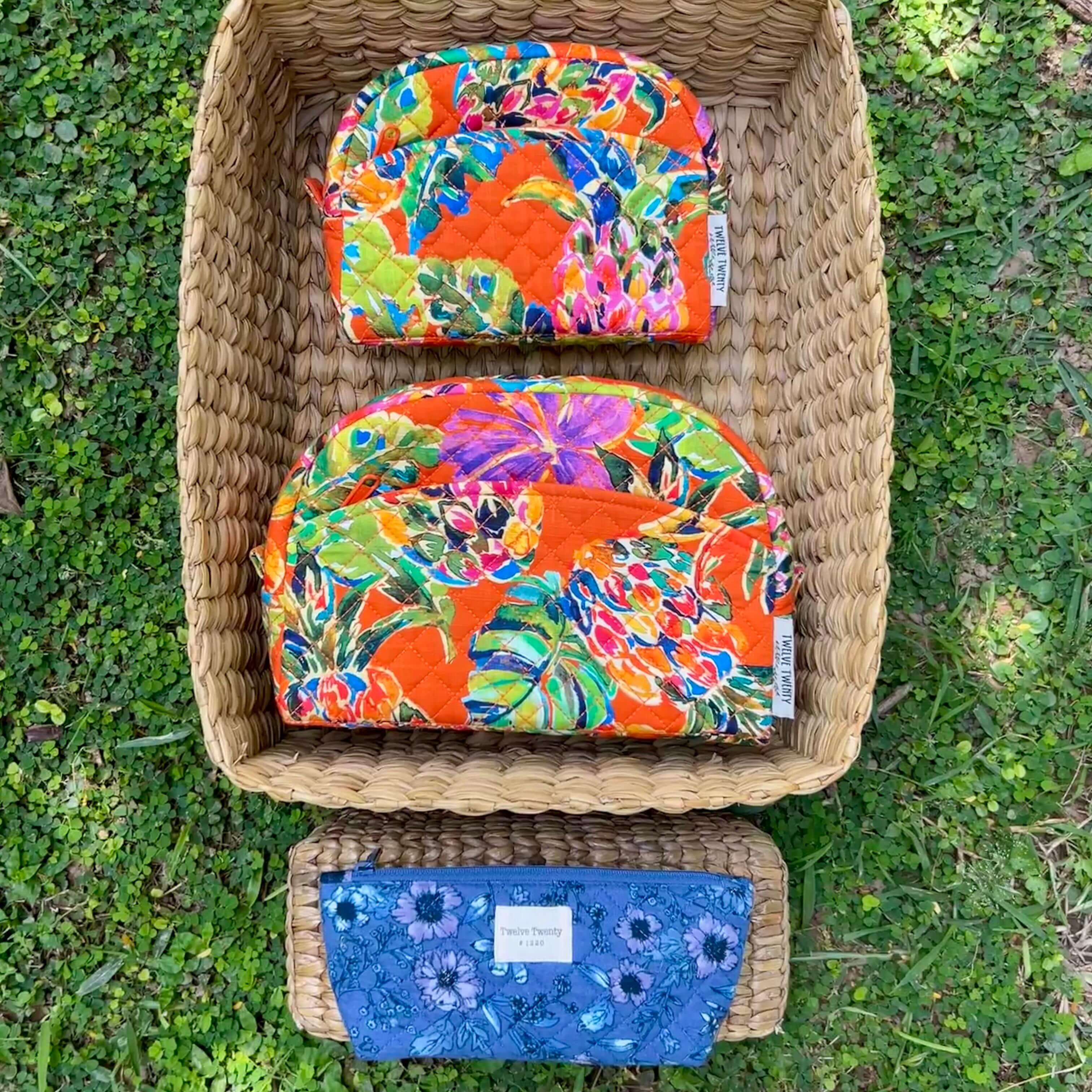 Colorful Trinity set of 3 makeup bags and everyday pouch in a woven basket on grass.